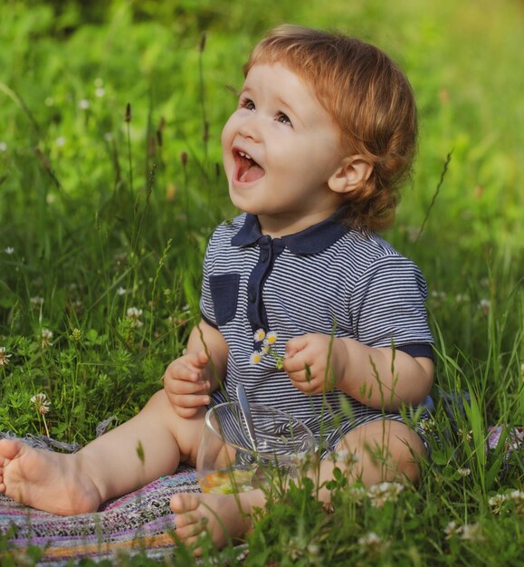 Criança bebê na grama no campo no verão, uma criança animada e bonita sentada ao ar livre