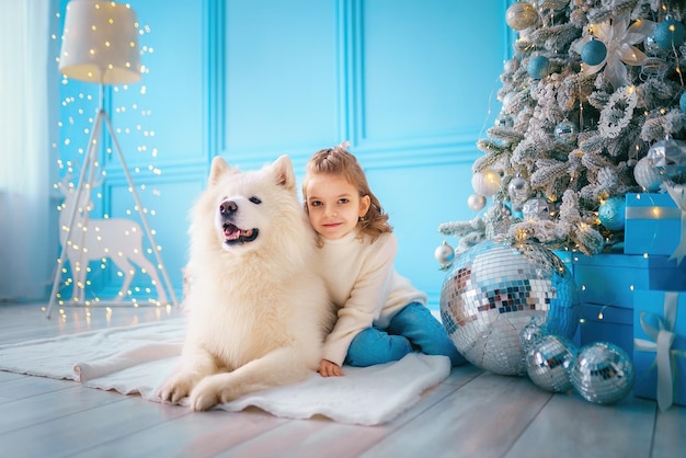 Criança bonita abraça cachorro malamute enquanto está sentado perto da árvore de natal na sala de estar Conceito de ano novo