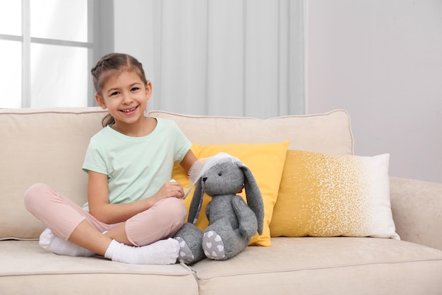 Criança bonita brincando de médico com bicho de pelúcia no sofá no hospital