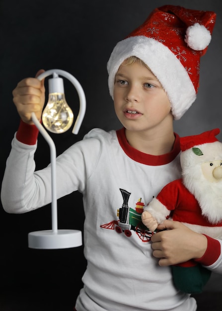 Criança bonita com chapéu de Papai Noel segurando a lanterna e um pouco de Papai Noel em fundo escuro, Natal