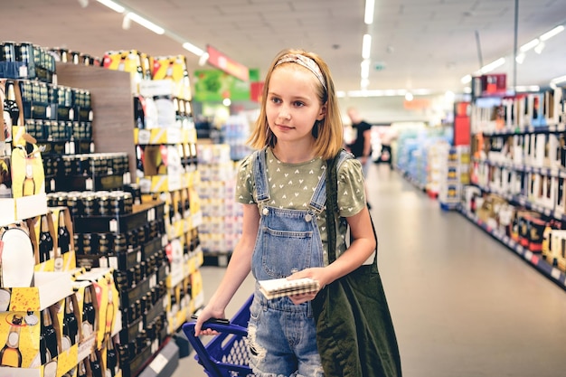 Criança bonita comprando com lista de compras no supermercado bela menina pré-adolescente em bebidas alcoólicas