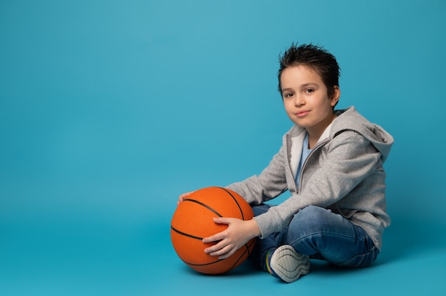 Criança bonita, jogador de basquete, sentada perto de uma bola