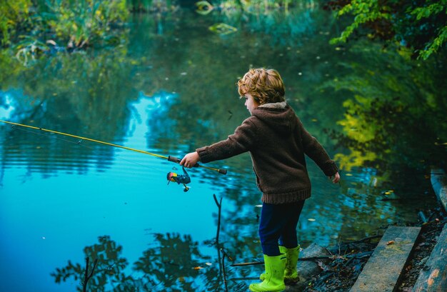 Foto criança bonita, um menino puxando uma vara enquanto pesca no lago