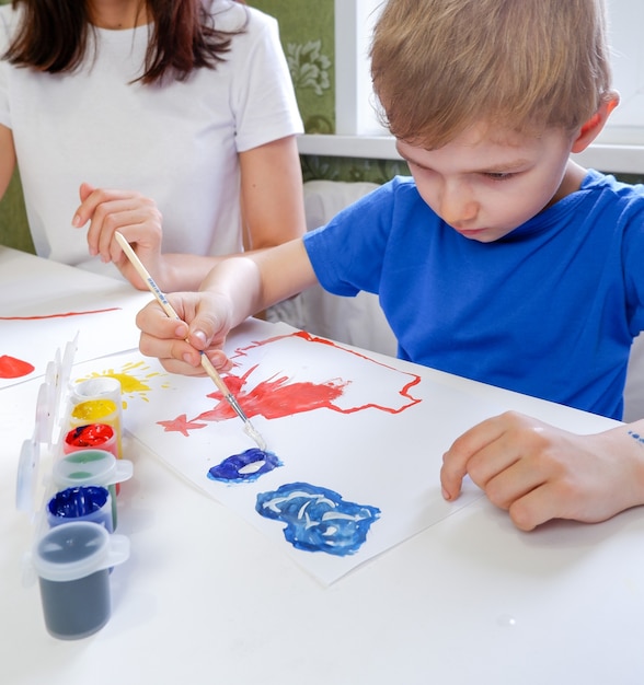 Criança bonitinha desenha à mesa com tintas com sua mãe closeup Sala de jogos