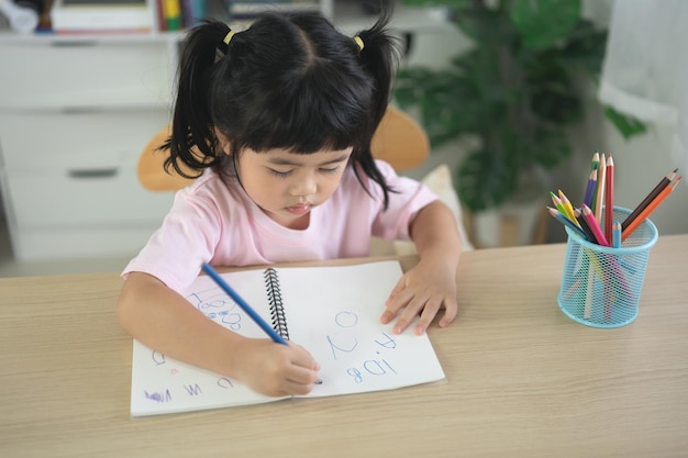 Criança bonitinha vestindo camisa rosa segurando lápis ou fazendo lição de casa ou pintura de cor de madeira com tintas coloridas Menina asiática usando cor de desenho de cor de madeira Conceito de estilo de vida de atividade de artista de bebê