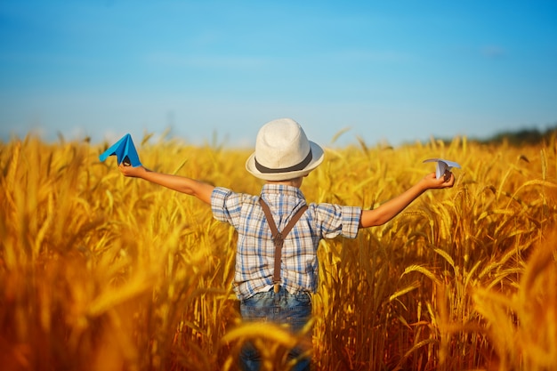 Criança bonito que anda no campo dourado do trigo em um dia de verão ensolarado. garoto começa o avião de papel. natureza no país.vista de fundo