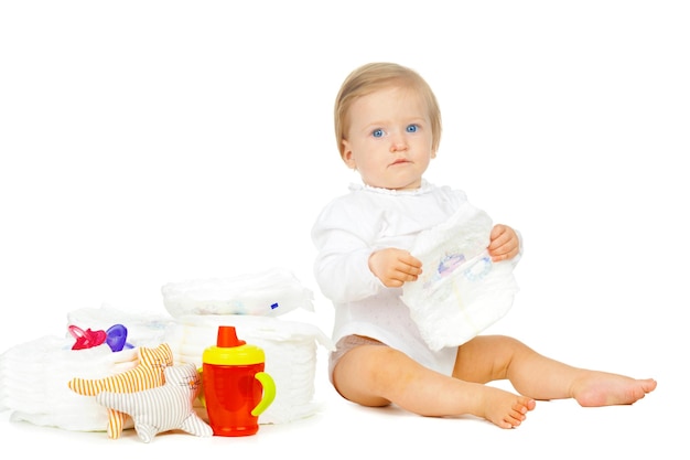 Criança branca com fraldas empilhadas e brinquedos isolados no fundo branco