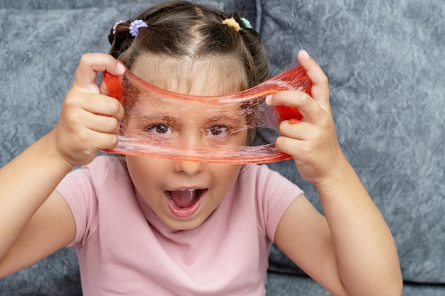 Criança brincando com limo vermelho, gunge, gel nas mãos