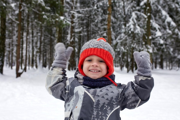 Criança brincando com neve no inverno garotinho de jaqueta colorida e chapéu de malha pegando flocos de neve em winter park no natal crianças brincam e pulam na floresta de neve crianças pegam flocos de neve