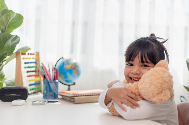 Criança brincando com ursinho de pelúcia Menina asiática abraçando seu brinquedo favorito Criança e bicho de pelúcia em casa