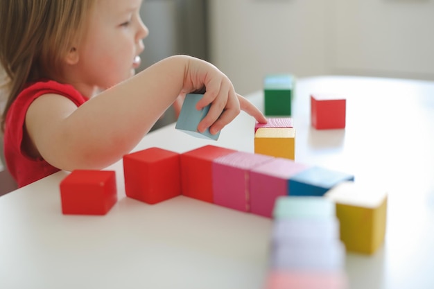 criança brincando e construindo com tijolos de brinquedo de madeira coloridos na mesa de madeira branca Aprendizagem precoce