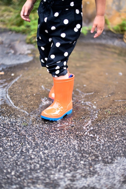 criança brincando em uma poça em botas de borracha após a chuva de verão