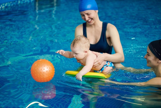 Criança brincando na piscina Bebê ficando na água a bordo tentando pegar bola de borracha laranja em água azul