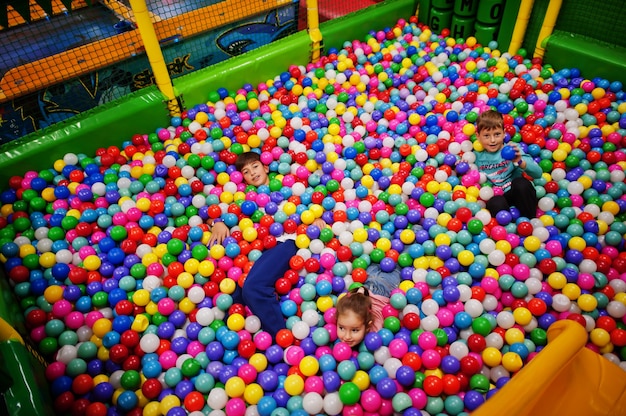 Criança brincando na piscina de bolinhas coloridas. Parque infantil interno da creche. Bilhar de bolas para crianças. Jardim de infância ou sala de jogos pré-escolar.