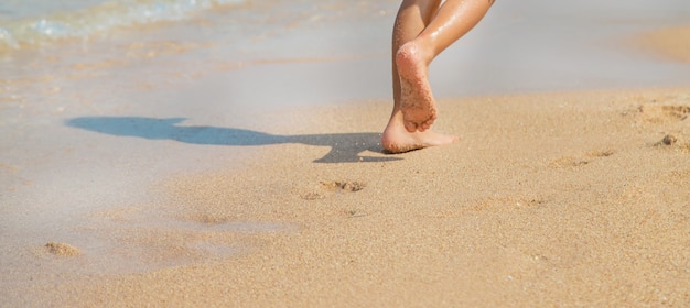 Criança caminha ao longo da praia deixando pegadas na areia.