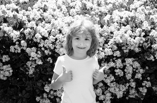 Criança caucasiana em flor de primavera fundo crianças com os polegares para cima