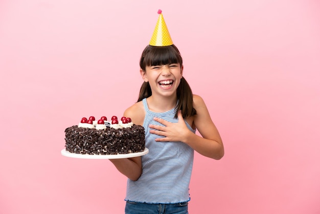 Criança caucasiana segurando bolo de aniversário isolado em fundo rosa sorrindo muito