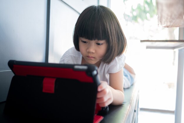 Criança chinesa viciada em tablet, menina asiática jogando smartphone, criança assistindo desenho animado