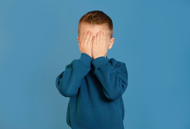 Criança cobrindo os olhos com as mãos isolado em fundo azul eu não quero ver nada menino assustado