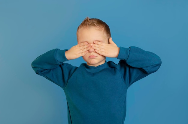 Foto criança cobrindo os olhos com as mãos isolado em fundo azul eu não quero ver nada menino assustado