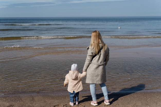 Criança com a mãe brincando à beira-mar em clima frio