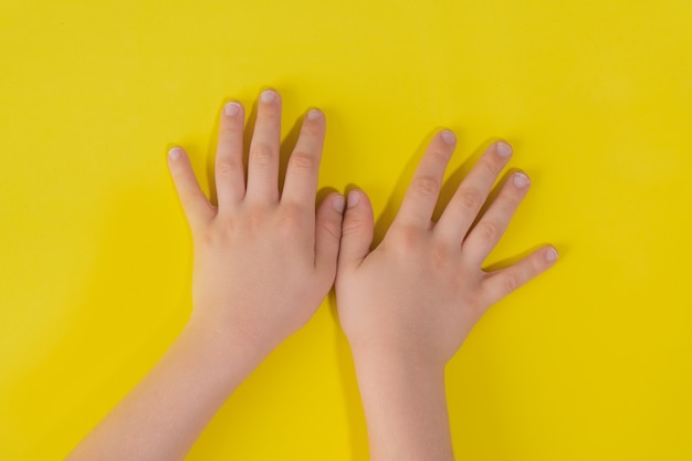 Criança com as mãos na superfície amarela