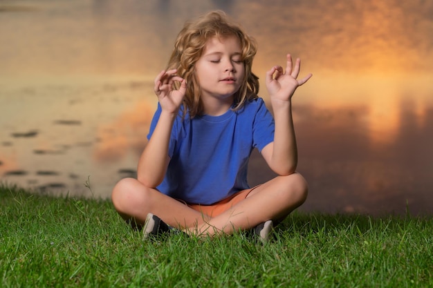 Criança com atenção plena meditando, sente-se na grama para paz e ioga, relaxe nos sóis de verão