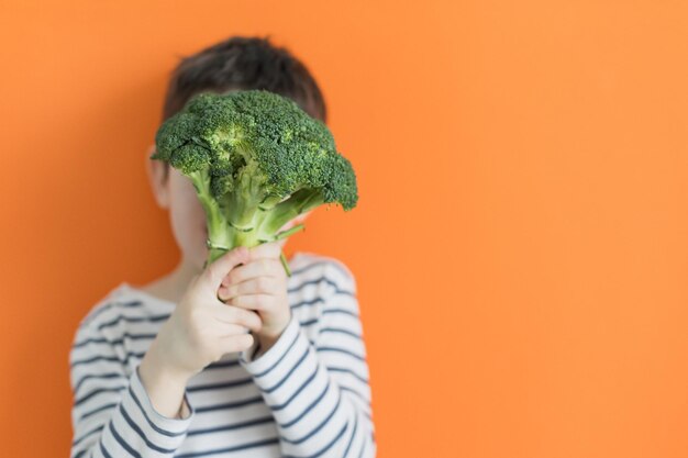 Criança com brócolis vegetal verde em um fundo laranja com espaço de cópia Conceito de comida saudável mercado agrícola de legumes frescos