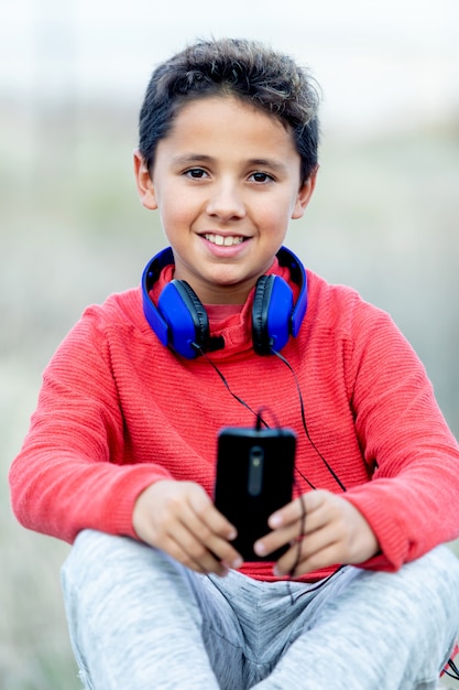 Criança com cabelo escuro, ouvindo música com hadphones azuis e um celular