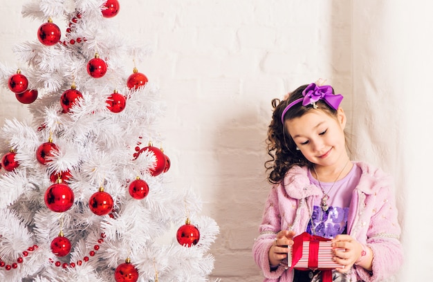 Criança com caixa de presente perto de árvore de Natal branco