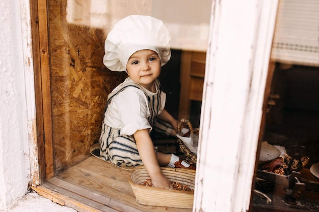 Criança com chapéu de chef e avental perto da janela