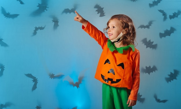 Criança com fantasia de carnaval de abóbora e máscara médica aponta com a mão em morcegos no Halloween