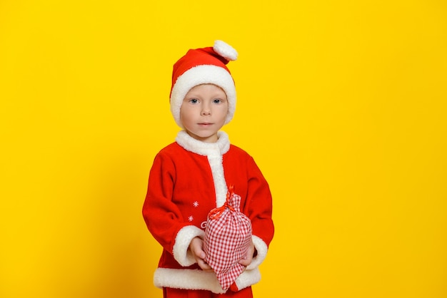 criança com fantasia de Papai Noel de Natal e uma barba branca segurando a ruiva em uma sacola branca com presentes