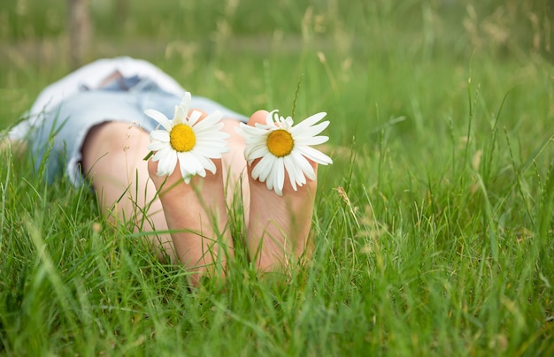 Criança com margarida deitada em um prado ensolarado e relaxando sob o sol de verão