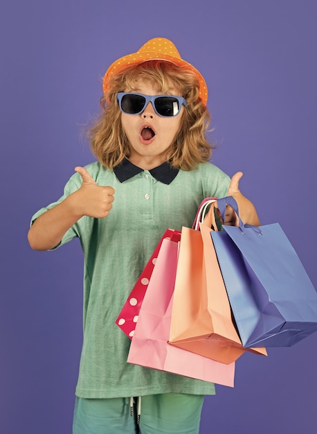 Criança com roupas da moda vai às compras Garoto com pacotes de compras Criança compradora carregando sacolas de compras