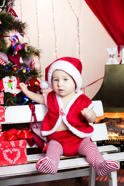 Criança com roupas de ano novo, passa o tempo na árvore de natal