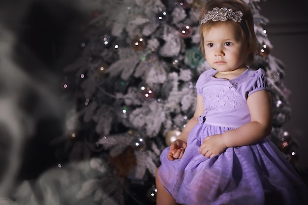 Criança com roupas elegantes na frente da árvore de Natal. Véspera de Ano Novo. Esperando pelo novo ano.