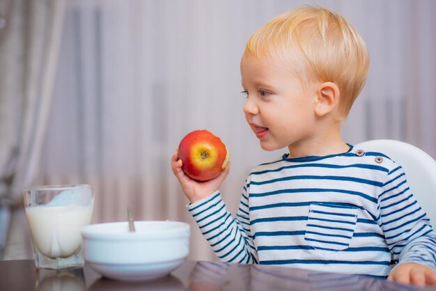 Criança come mingau garoto bonitinho olhos azuis sentados à mesa com prato e comida comida saudável menino bonitinho