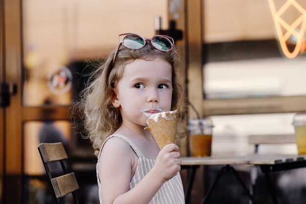 Criança comendo casquinha de sorvete perto de um café na rua