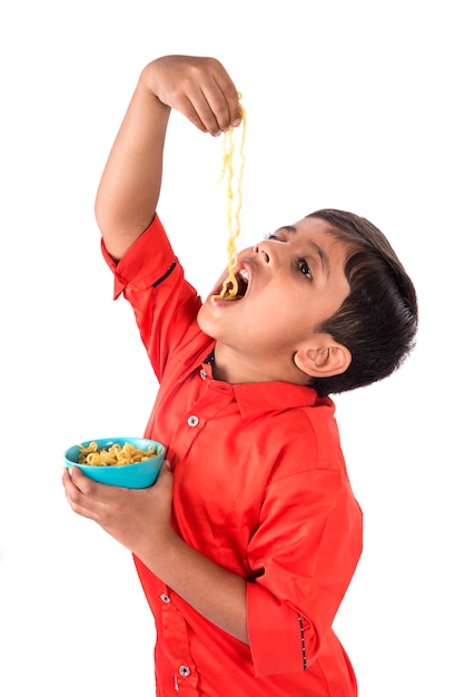 Criança comendo macarrão delicioso, garoto indiano comendo macarrão com garfo na parede branca