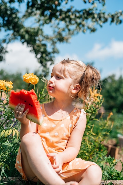 Criança comendo melancia no jardim. as crianças comem frutas ao ar livre. lanche saudável