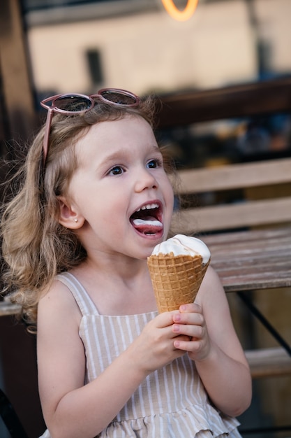 Criança comendo sorvete de casquinha do lado de fora perto de um café comidas congeladas de verão