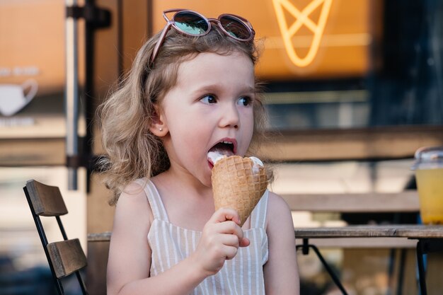 Criança comendo sorvete de casquinha do lado de fora perto de um café comidas congeladas de verão