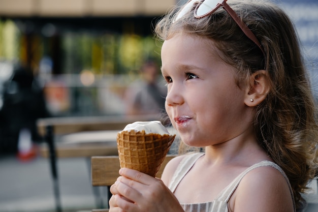 Criança comendo sorvete de casquinha do lado de fora perto de um café comidas congeladas de verão