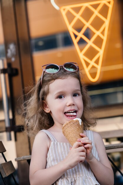 Criança comendo sorvete de casquinha do lado de fora perto de um café comidas congeladas de verão