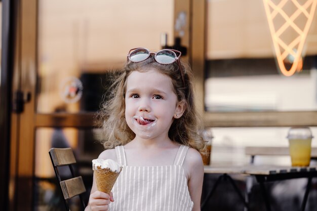 Criança comendo sorvete de casquinha do lado de fora perto de um café comidas congeladas de verão