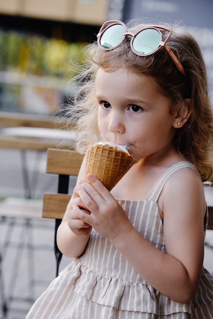 Criança comendo sorvete de casquinha do lado de fora perto de um café comidas congeladas de verão