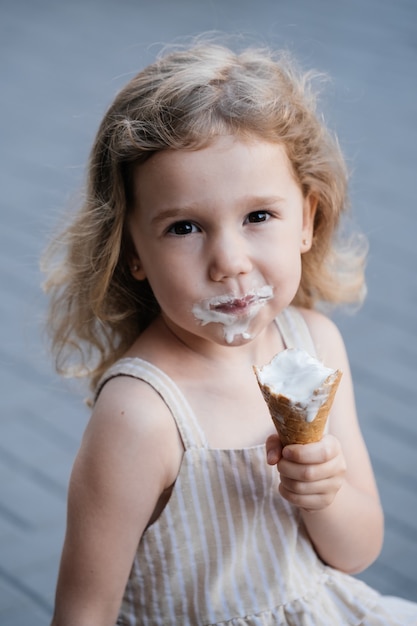 Criança comendo sorvete de casquinha do lado de fora perto de um café comidas congeladas de verão