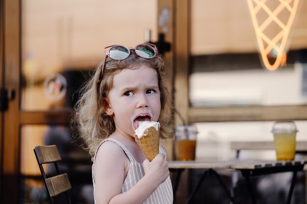 Criança comendo sorvete de casquinha do lado de fora perto de um café comidas congeladas de verão
