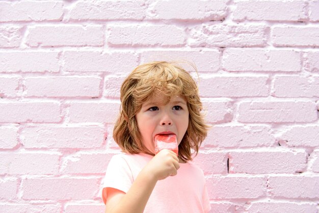 Criança comendo sorvete em um fundo de parede rosa.